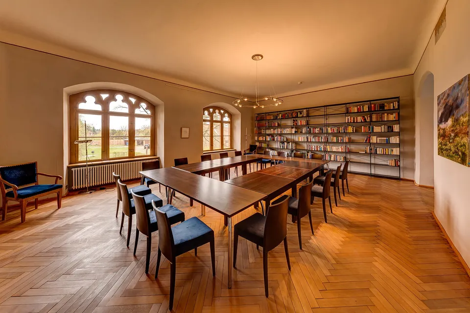 An empty meeting room with a long wooden table, chairs and bookshelves under arched windows