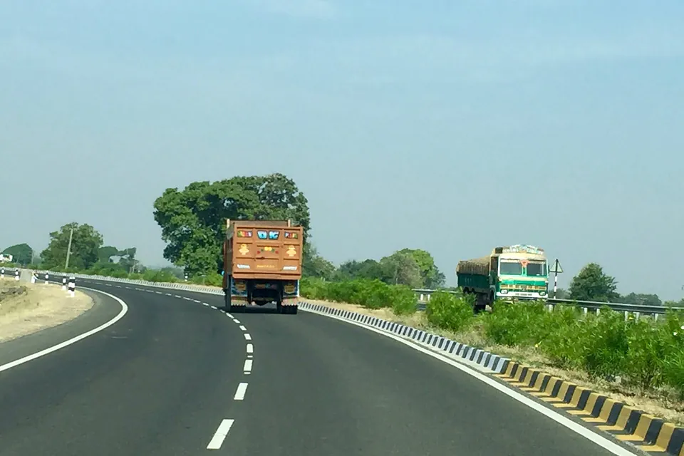 Two goods lorries on a curving divided highway lined with trees in Gujarat, India