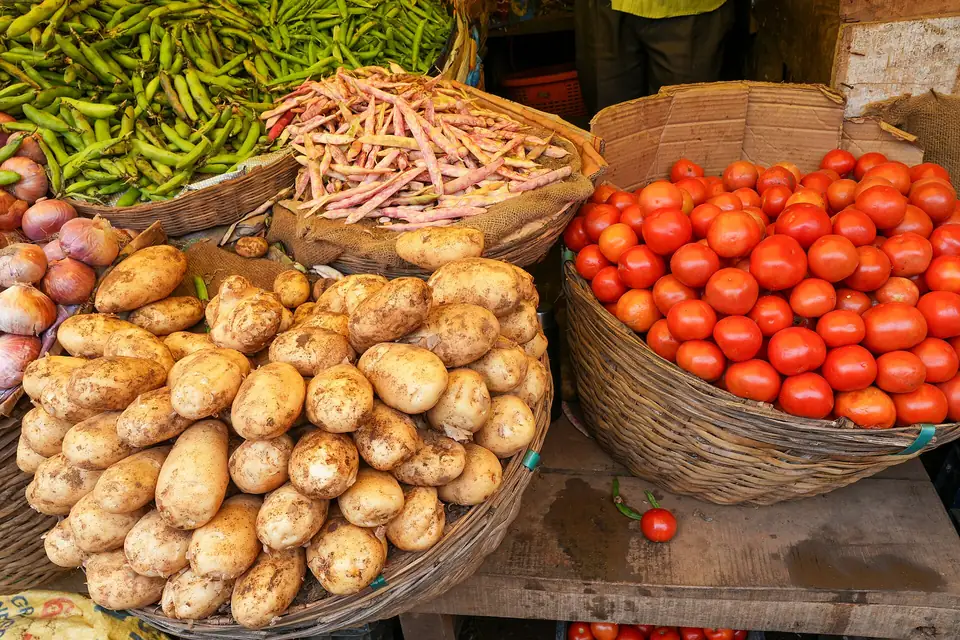 Baskets of potatoes, tomatoes and green beans piled on a market stall